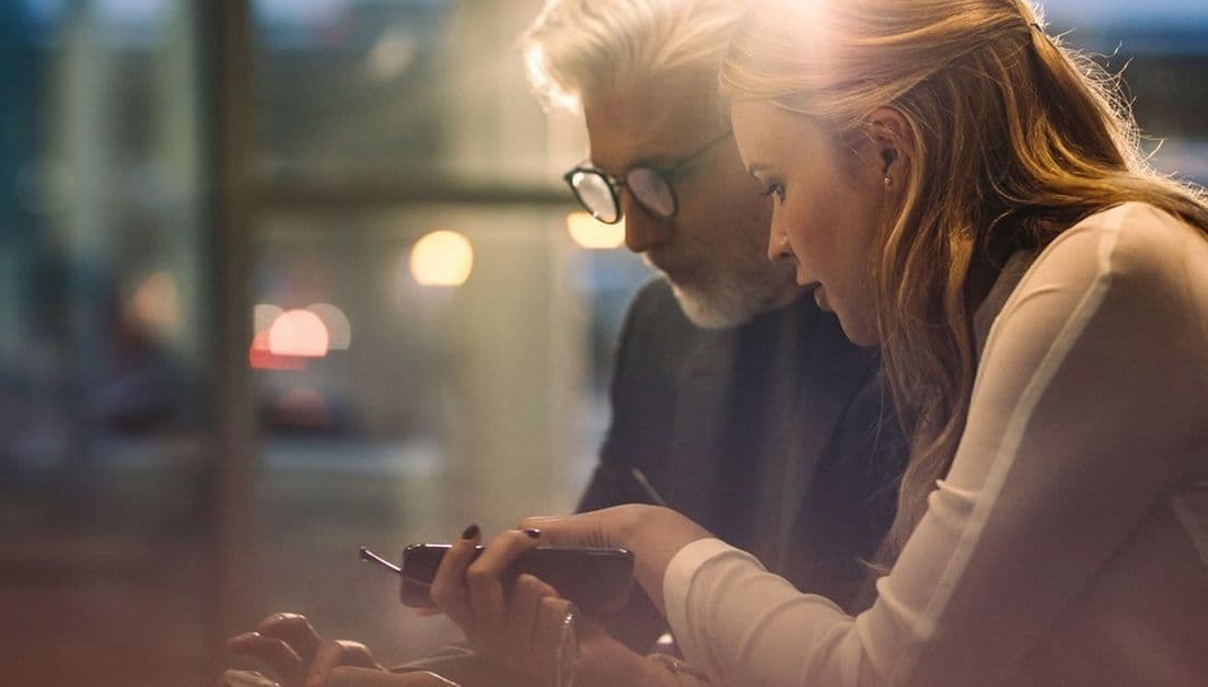 Man och kvinna med smartphone sitter bredvid varandra och  diskuterar i jobbsammanhang..